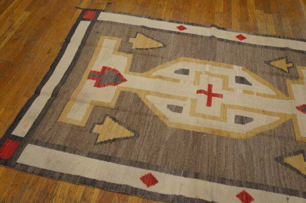 Brown, cream, and gold geometric rug with red motifs lying on distressed wooden floors.