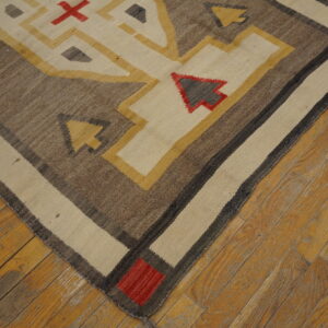 Geometric flatweave rug in brown, cream, yellow, and red colors shown on rustic wood planks.