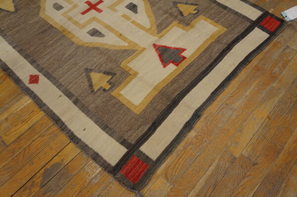 Geometric flatweave rug in brown, cream, yellow, and red colors shown on rustic wood planks.