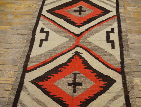 Cream, coral, and dark brown geometric runner rug with cross motifs lying on light plank flooring.