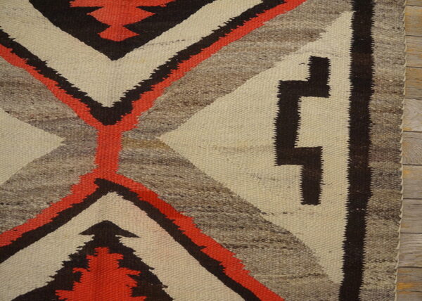 Geometric, low-pile rug featuring bold stepped patterns in cream, coral, dark brown, and heathered gray on a wood floor.