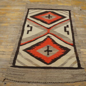 Geometric flatweave runner featuring dark brown, orange, and cream diamonds on worn, pale wood flooring.