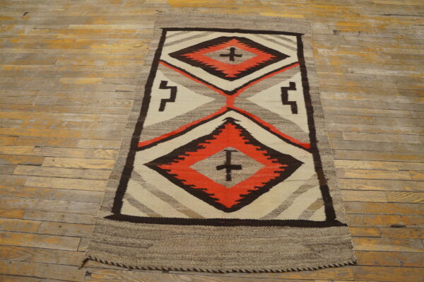 Geometric flatweave runner featuring dark brown, orange, and cream diamonds on worn, pale wood flooring.