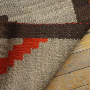 Geometric brown, beige, and orange rug detail with visible texture, partially folded on rustic wood planks.
