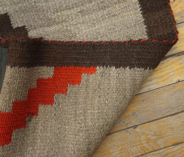 Geometric brown, beige, and orange rug detail with visible texture, partially folded on rustic wood planks.