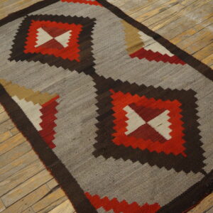 Geometric flat-woven rug featuring gray, dark brown, and red diamonds on distressed wood planks.