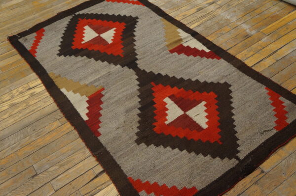 Geometric flat-woven rug featuring gray, dark brown, and red diamonds on distressed wood planks.