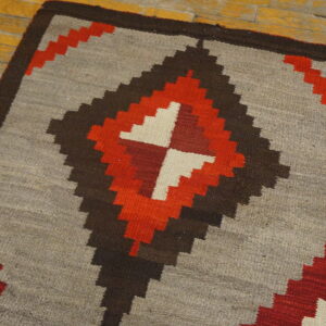 Gray flatweave rug with red, brown, and cream geometric stepped diamond design on wood planks.