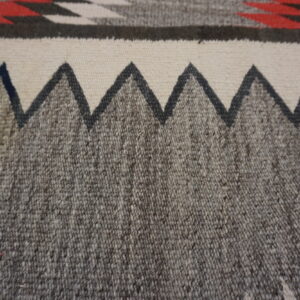 Close-up of a tightly woven rug showing a gray heathered field and a dark jagged border on cream.