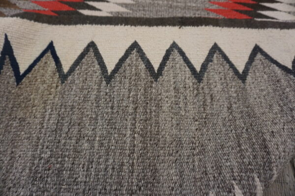 Close-up of a tightly woven rug showing a gray heathered field and a dark jagged border on cream.
