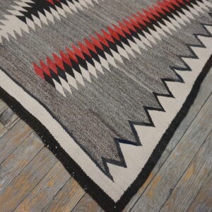 Geometric flatweave rug featuring zigzags in grey, cream, black, and red on weathered wood planks.