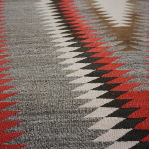 Flatweave rug detail showing sharp, interlocking geometric patterns in red, gray, black, and white.