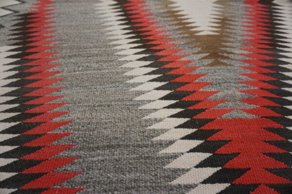 Flatweave rug detail showing sharp, interlocking geometric patterns in red, gray, black, and white.