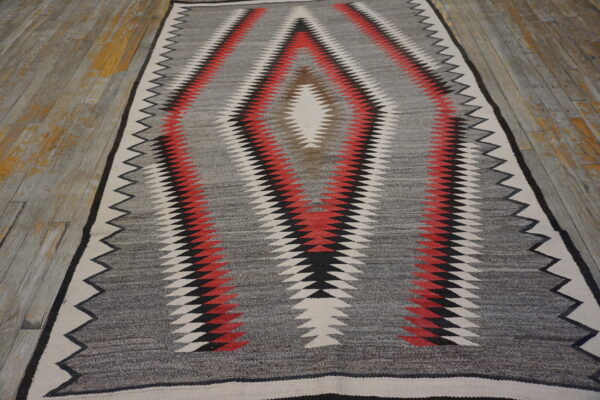 Gray, red, black, and white serrated diamond runner rug centered on rustic plank flooring.
