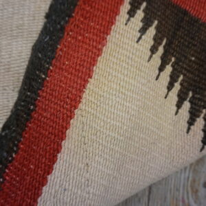 Detail of a flat-weave rug showing beige, red, and dark brown geometric stripes on wooden flooring.