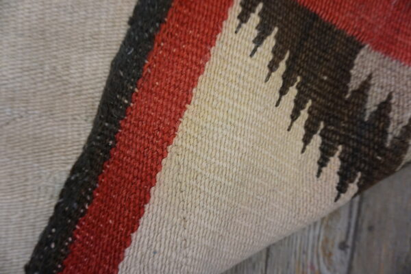 Detail of a flat-weave rug showing beige, red, and dark brown geometric stripes on wooden flooring.