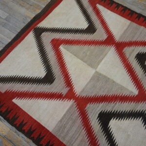 A flatweave rug with serrated geometric patterns in cream, red, gray, and dark brown on gray wood.