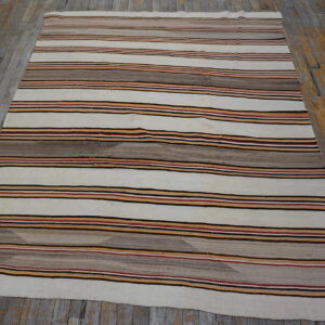 Off-white rug with horizontal stripes in brown, black, orange, and red on distressed wood floors.