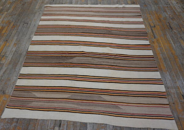 Off-white rug with horizontal stripes in brown, black, orange, and red on distressed wood floors.
