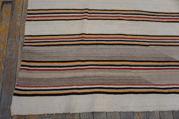 Cream and grey flat-weave rug featuring thin stripes of black, red, and yellow on wood flooring.