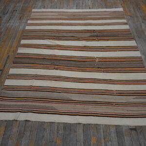 Striped flatweave rug in cream, brown, red, black, and orange colors rests on distressed wooden flooring.