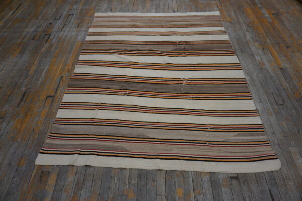 Striped flatweave rug in cream, brown, red, black, and orange colors rests on distressed wooden flooring.