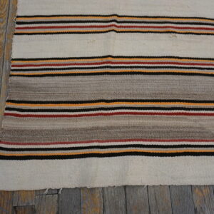 White and gray flatweave rug with orange, red, and black stripes on distressed plank flooring.