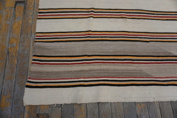 White and gray flatweave rug with orange, red, and black stripes on distressed plank flooring.