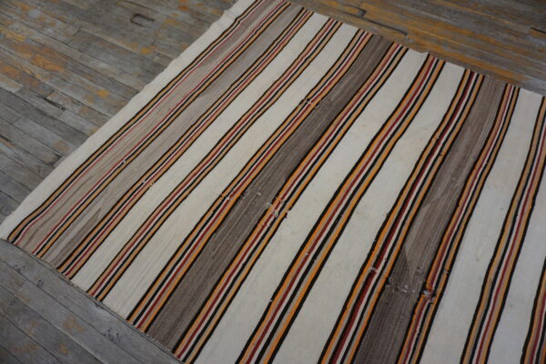 Striped flatweave rug featuring cream, gray, orange, red, and black on distressed gray plank flooring.