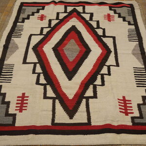Geometric flatweave rug in cream, black, red, and gray rests on weathered yellow-toned hardwood planks.