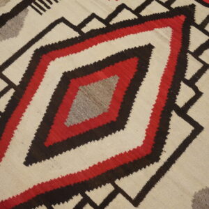 Cream, red, dark brown, and gray geometric flat-weave rug on rustic wood plank flooring.