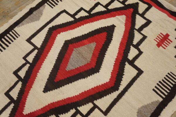 Cream, red, dark brown, and gray geometric flat-weave rug on rustic wood plank flooring.