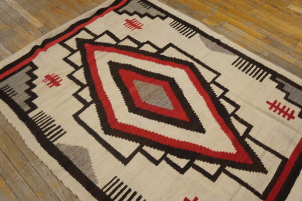 Cream, red, black, and gray flatweave rug featuring a large central concentric diamond design on wood flooring.
