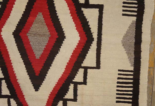 Red, brown, and gray geometric diamond patterns detail a cream low-pile rug resting on wood flooring.