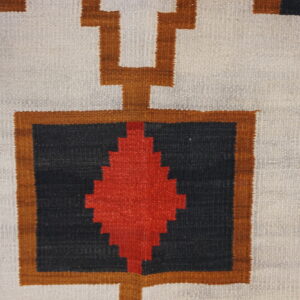 Geometric rug pattern featuring red, black, and brown designs on a textured off-white flatweave background.