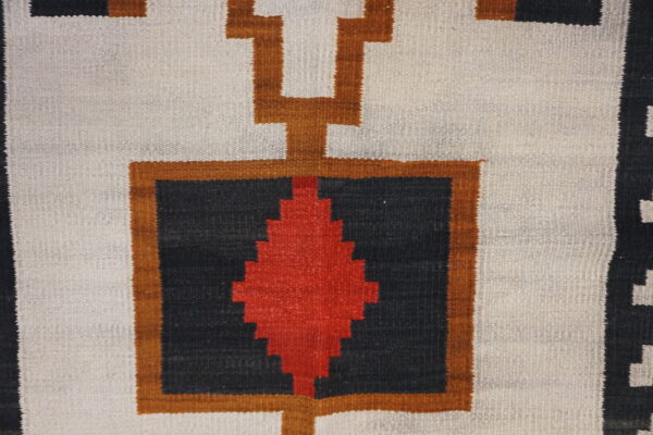 Geometric rug pattern featuring red, black, and brown designs on a textured off-white flatweave background.