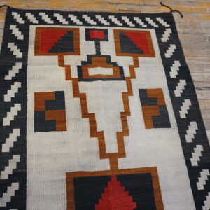 Geometric flatweave rug in black, white, red, and rust on rustic wood planks.