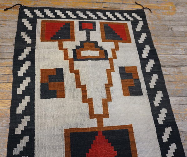 Geometric flatweave rug in black, white, red, and rust on rustic wood planks.