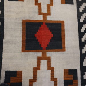 Geometric flatweave rug in white, black, red, and brown colors displayed on distressed wood planks.