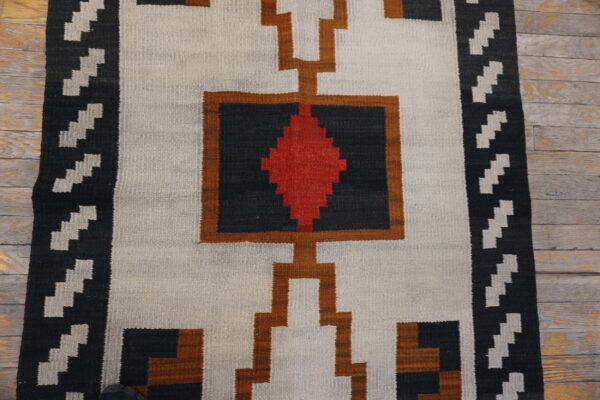 Geometric flatweave rug in white, black, red, and brown colors displayed on distressed wood planks.