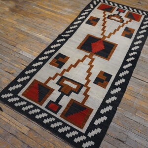Flatweave rug with a geometric design in black, light gray, red, and brown on weathered wood planks.