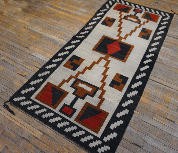 Flatweave rug with a geometric design in black, light gray, red, and brown on weathered wood planks.