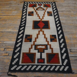 Geometric flatweave runner featuring black, white, brown, and red patterns on rustic wood flooring.
