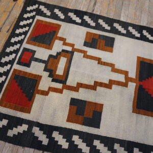 Geometric runner rug in white, gray, red, and rust colors on distressed yellow wood planks.
