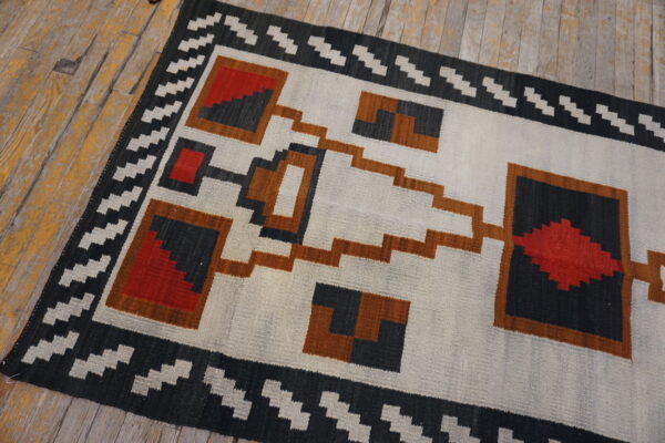 Geometric runner rug in white, gray, red, and rust colors on distressed yellow wood planks.