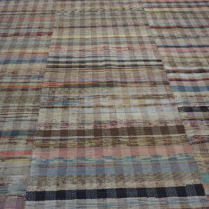 Multicolor flatweave rug with horizontal stripes and checkered patches on light wood planks.