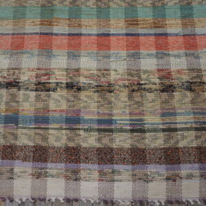 Multicolor rag rug with thick woven stripes and checkered sections on distressed gray wood floor.