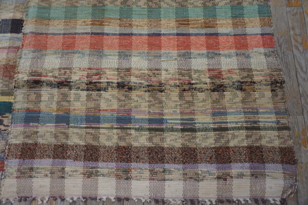 Multicolor rag rug with thick woven stripes and checkered sections on distressed gray wood floor.