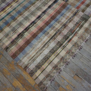 A colorful patchwork striped flatweave rug rests on weathered gray and yellow wood flooring.