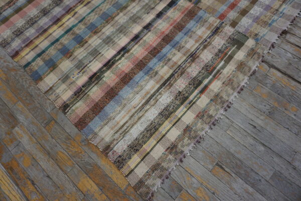 A colorful patchwork striped flatweave rug rests on weathered gray and yellow wood flooring.
